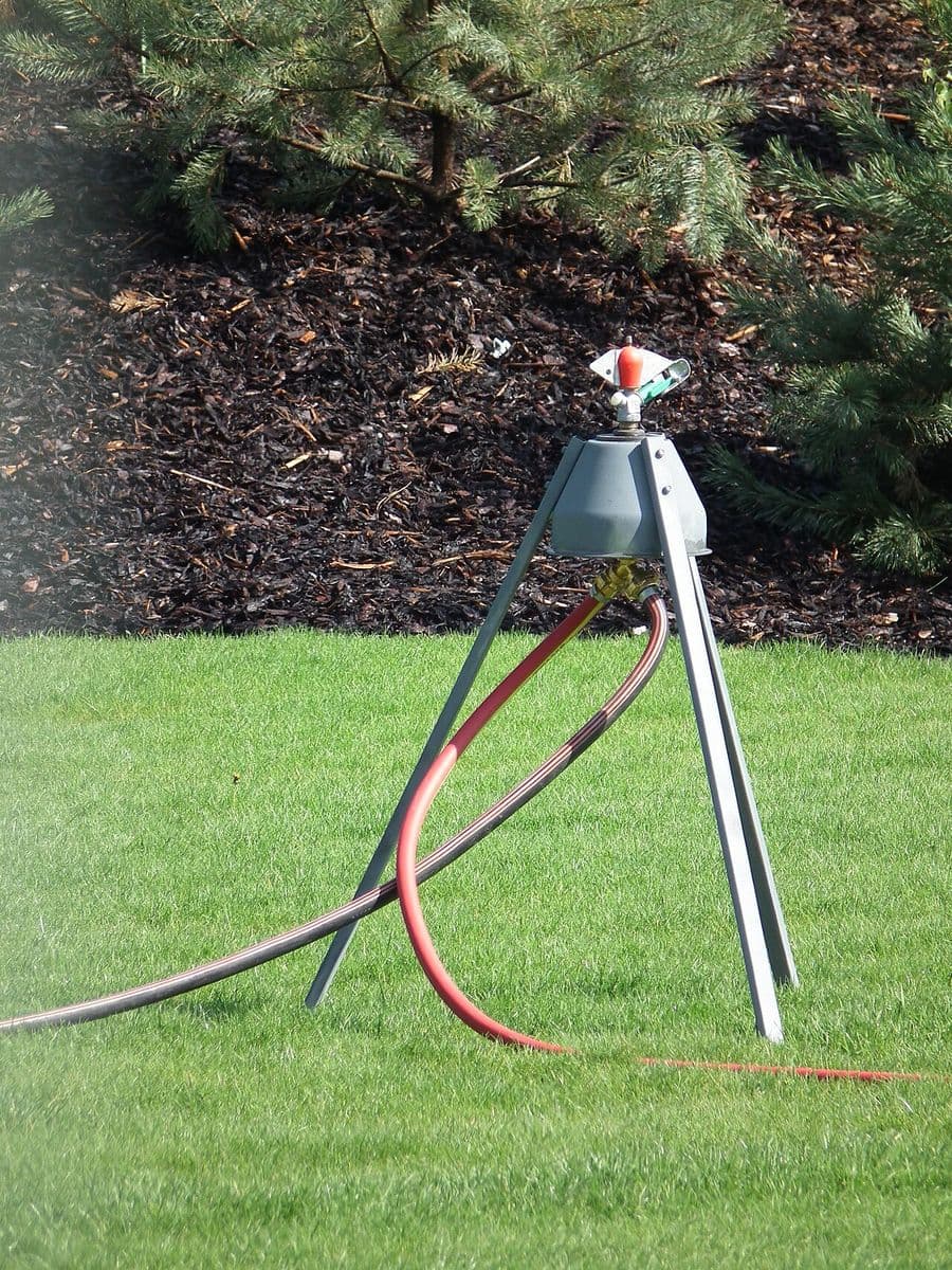 A sprinkler watering a healthy green lawn beside a mulched bed